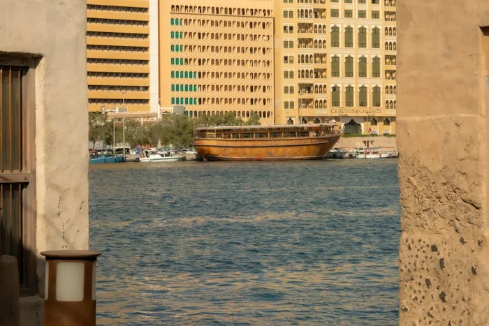 A traditional wooden dhow on Dubai Creek with old and new buildings behind