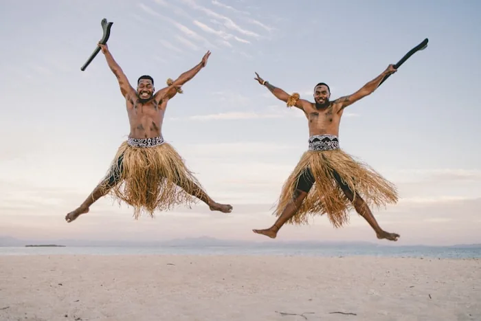 Two Fijian men in traditional grass skirts on the beach