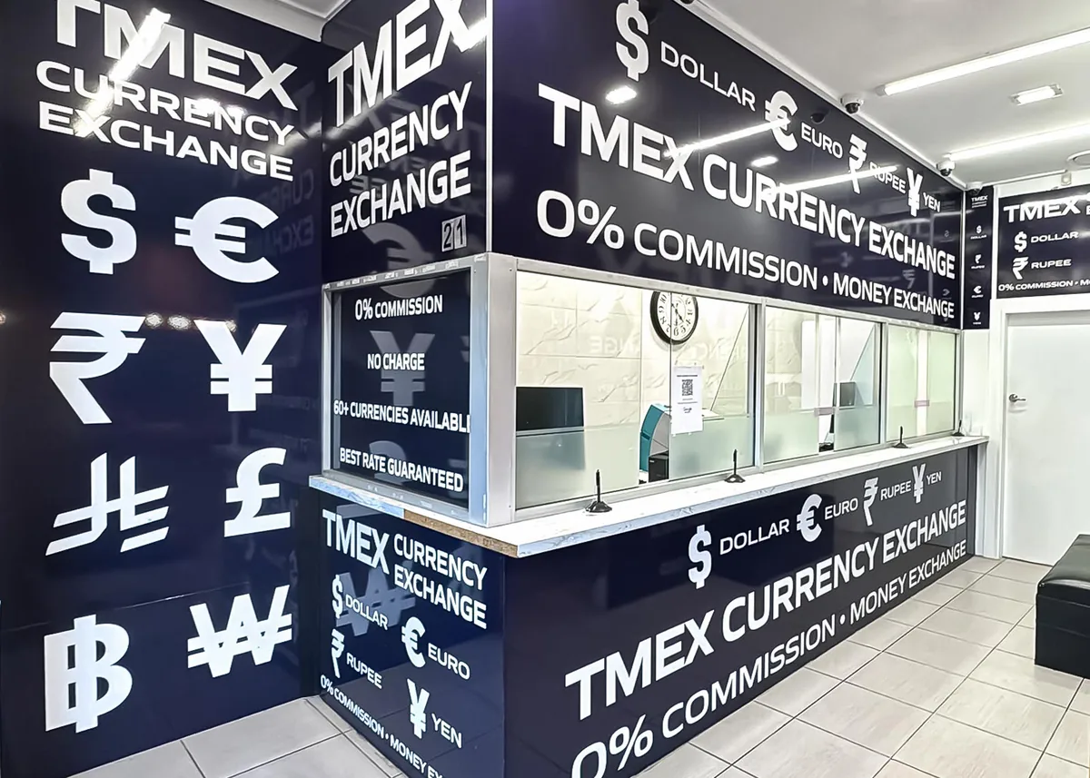 Inside the TMEX Currency Exchange store in Auburn, showing the service counter, the glass screens and the wall of world currency symbols.