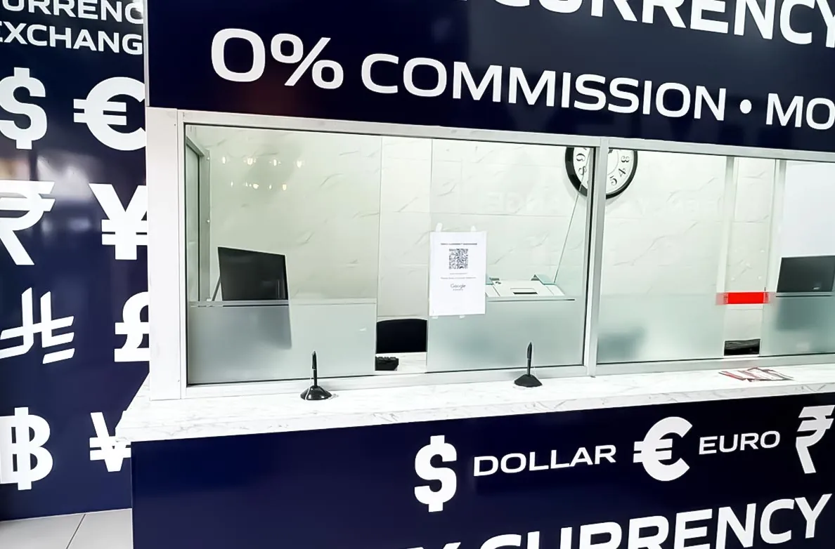 The TMEX Currency Exchange service counter in Auburn, with the note-counting machine behind the glass and the 0% commission sign above.